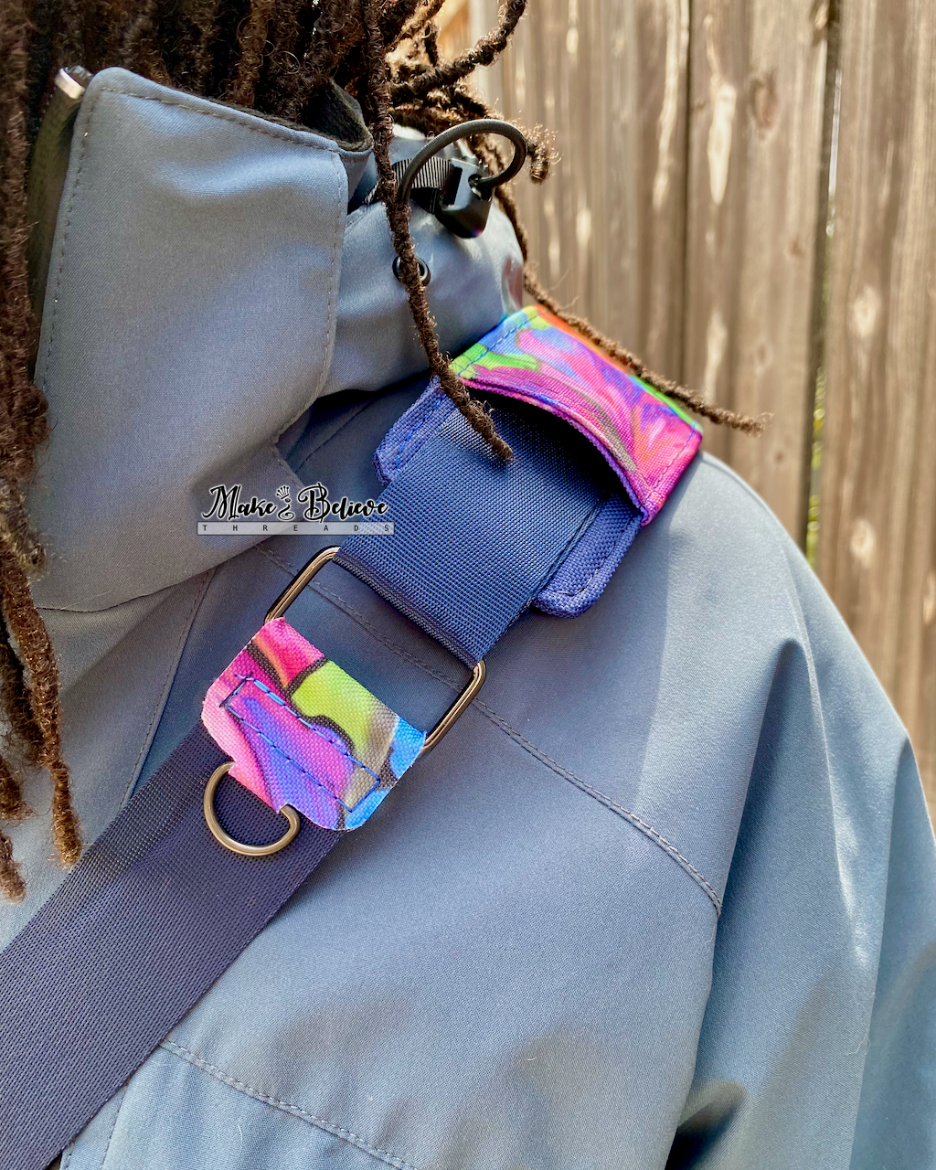 Close-up of a 1.5" navy blue crossbody strap with a floral print shoulder pad and a d-ring connector for attaching clipped items.