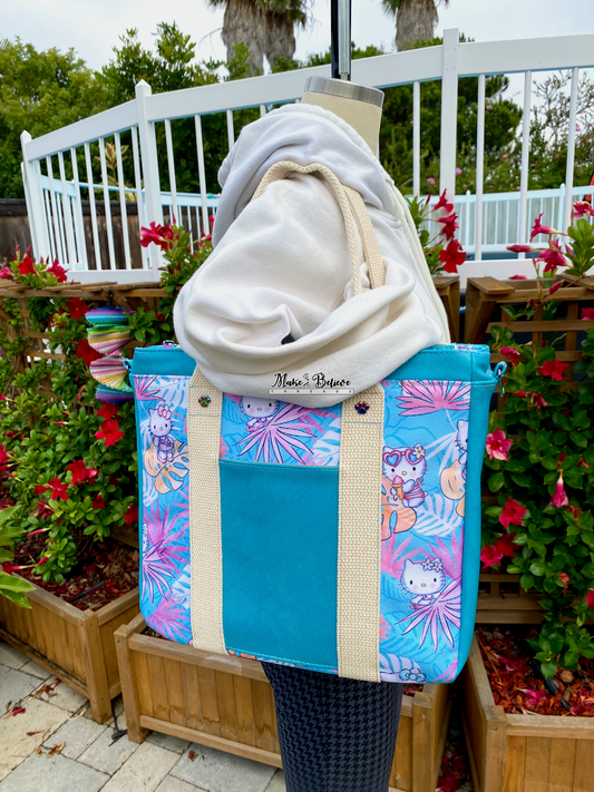 Mannequin holding Aqua blue tote bag with pink and blue tropical print featuring "Bow Kitty," photographed outdoors.