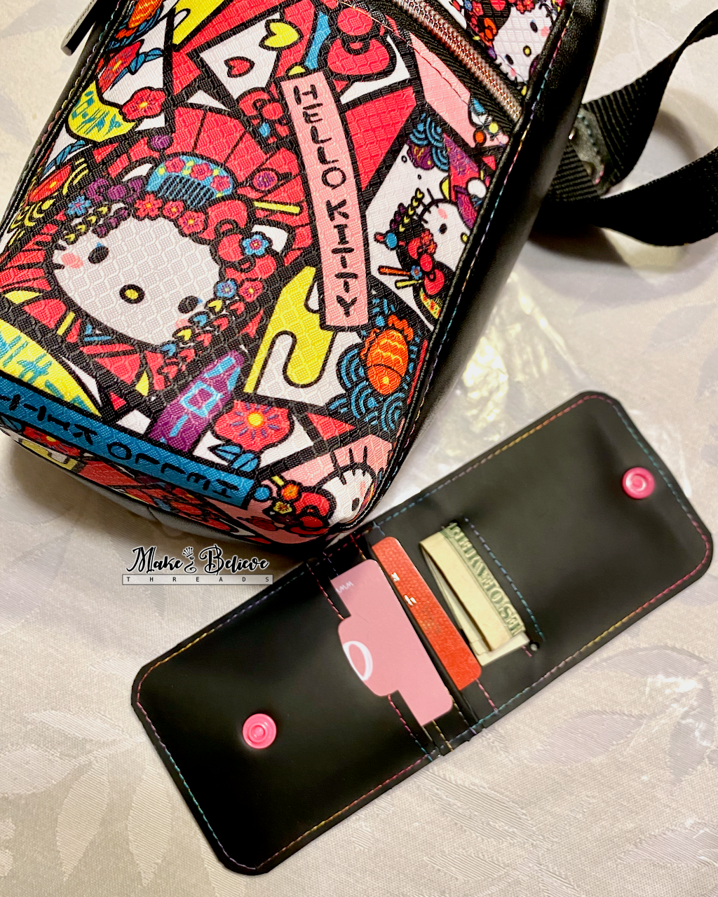Colorful "Bow Kitty" water bottle carrier laying on table next to an open black jelly vinyl wallet showing cards and cash on a light background