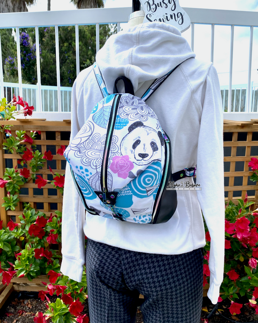 Mannequin wearing a white hoodie with a panda-themed backpack in front of a wooden fence and flowers.