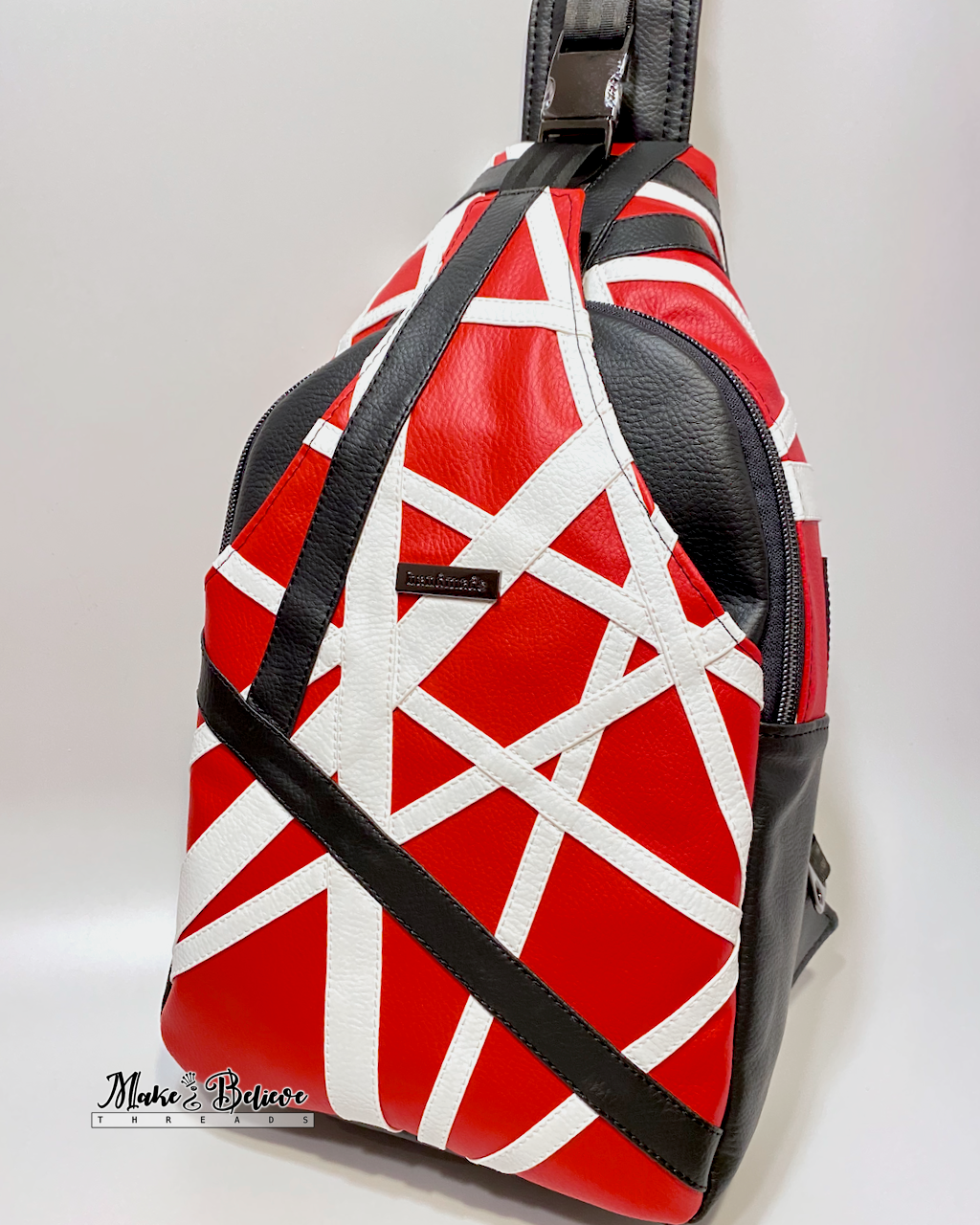 Red, white, and black sling bag on a light gray background. The geometric appliqué design is patterned after Eddie Van Halen's Frankenstrat.