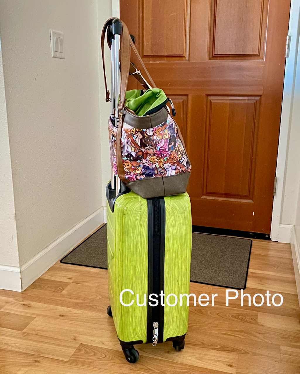 Green suitcase with a cartoon cats travel tote slipped on top in front of a wooden door