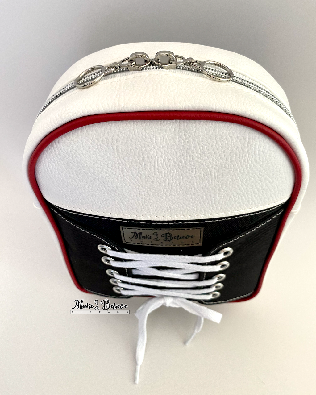 Above view of zipper gusset on a black and white sneaker-shaped bag with white laces on a light gray background