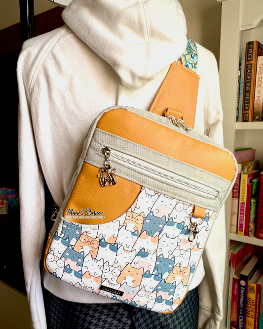Sling bag with cat pattern and orange top section, worn by a mannequin in a white hoodie.