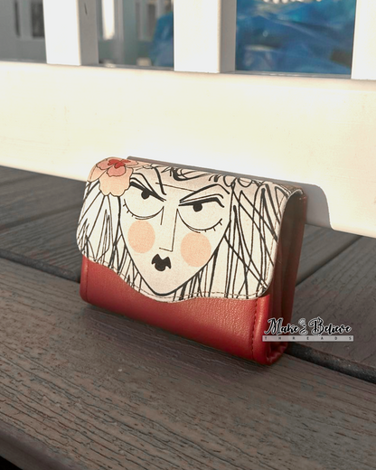Mini Necessary Clutch Wallet on wooden surface with artistic face on flap from Alexander Henry's Ghastlies collection