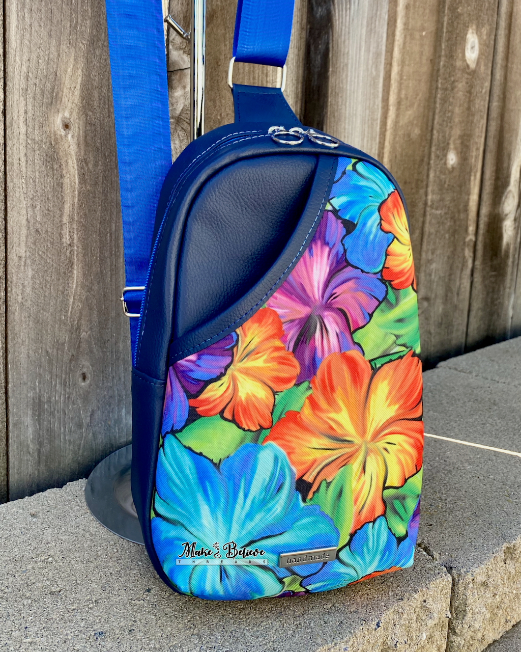 Floral-patterned sling bag with navy exterior and blue strap on a stone surface against a wooden background
