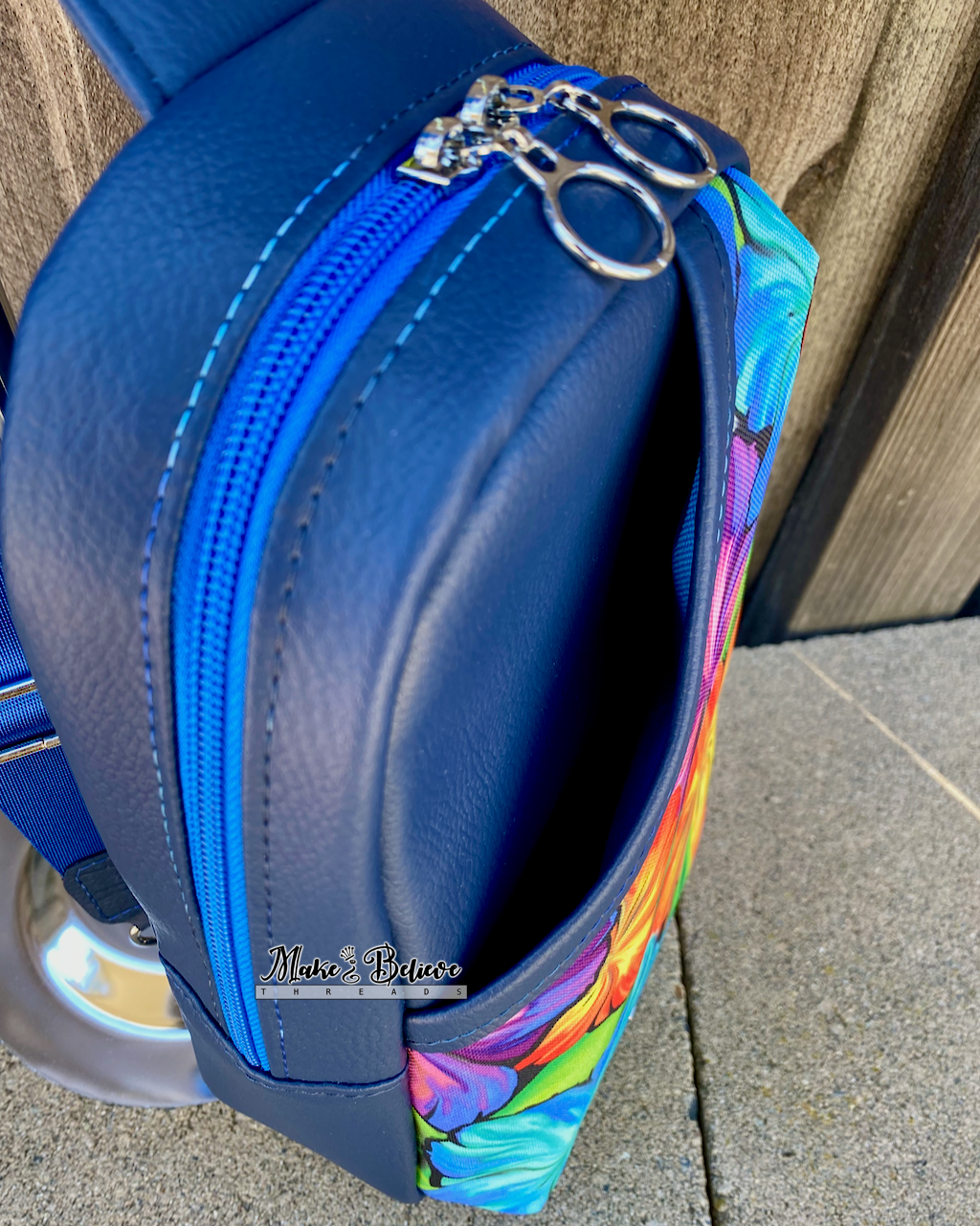 Above view of floral-patterned sling bag with navy exterior showing the opening of a front exterior slip pocket, photographed on a stone surface against a wooden background