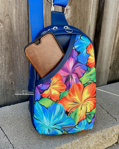 A navy sling bag with with a phone peeking out of a floral patterned front slip pocket, photographed on a stone surface in front of a wooden fence
