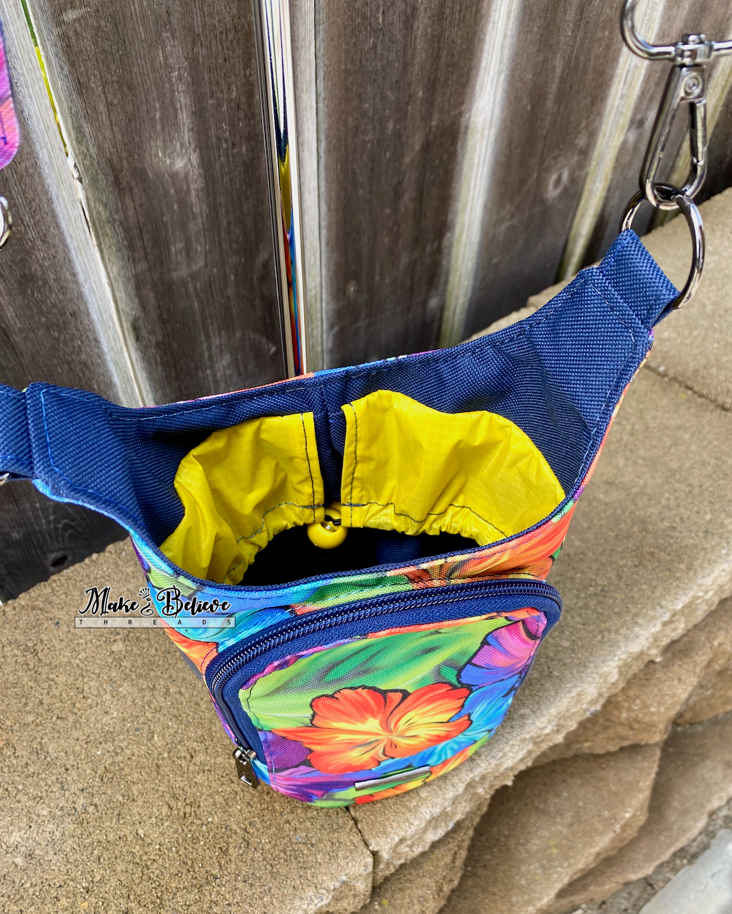 Interior of colorful floral pattern water bottle carrier showing a yellow tucked in drawstring closure  photographed on a stone wall in front of a wooden fence.