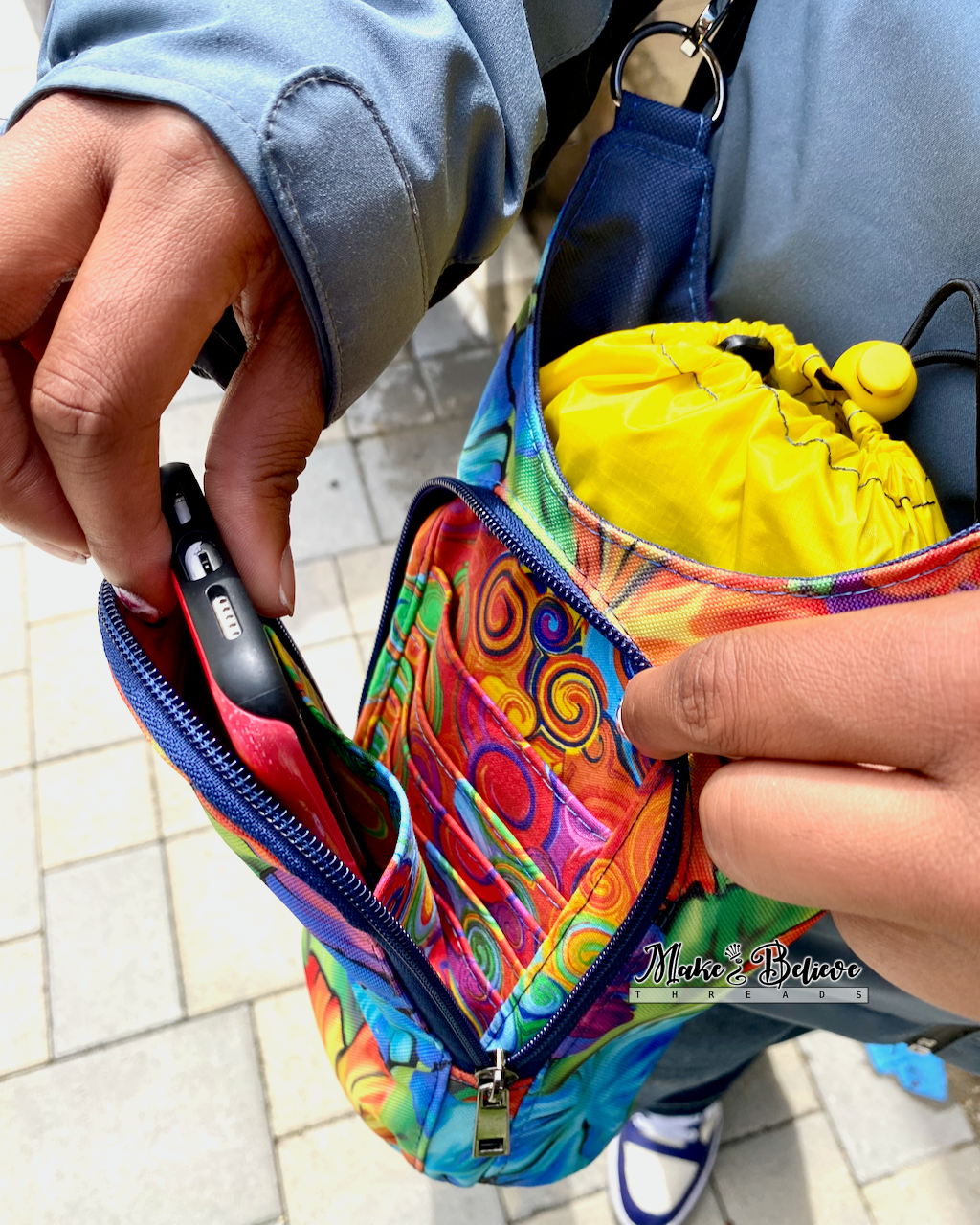 A person is sliding a phone into one of the slip pockets in the front pouch of a colorful water bottle carrier.