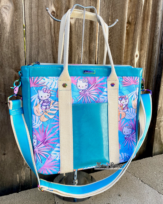 Aqua blue tote bag with pink and blue tropical print featuring "Bow Kitty" in front of a wooden fence.