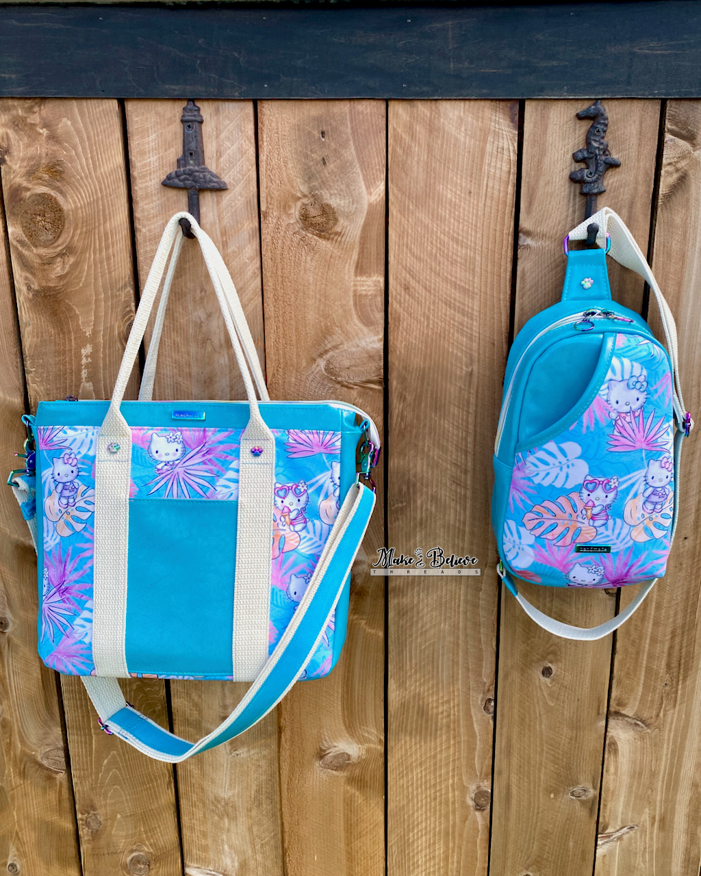 An aqua blue tote bag with pink and blue tropical print featuring "Bow Kitty" next to a matching sling bag, both hanging from a wooden fence.