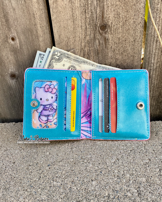 Interior of a blue wallet with "Bow Kitty," money, and cards against a wooden fence background