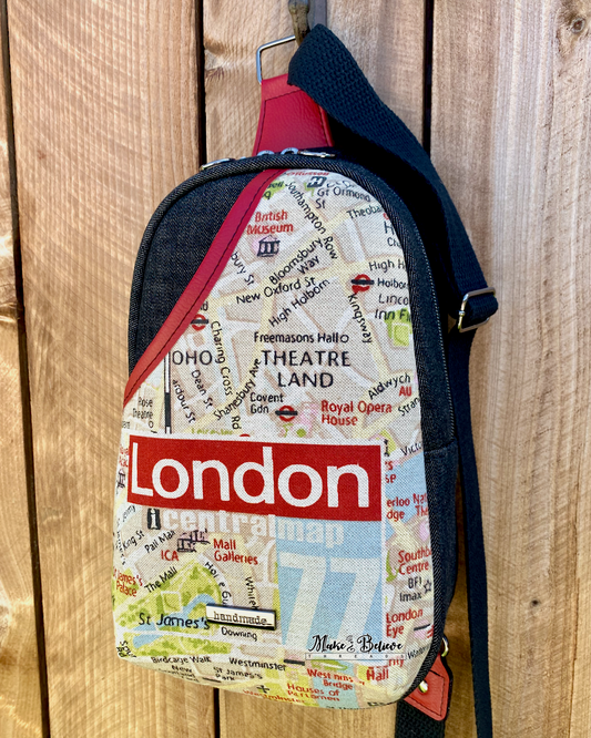 London map-patterned sling bag with black denim exterior and strap against a wooden background.
