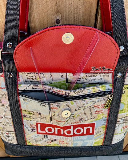 Black denim tote with red accents and map-pattern with 'London' text on a wooden surface. Photo illustrates an open front flap pocket revealing a slip pocket and zipper pocket.