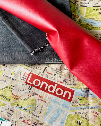 Three piles of fabric used to construct a tote bag: Pebbled red faux leather, black denim, and a printed canvas detailing a map of London.