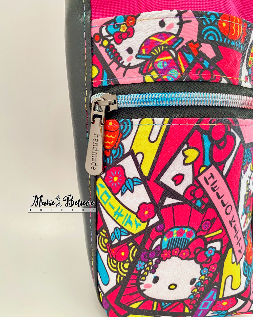 Close-up view of the "Bow Kitty" ripstop fabric, a  zipper pull that reads 'handmade', and rainbow coloured stitching