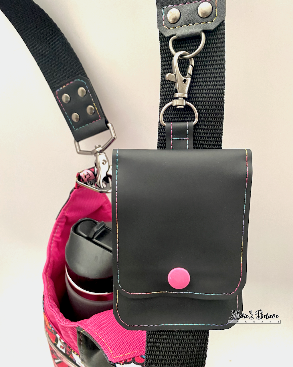 Front of a black jelly vinyl flip wallet with pink plastic snap attached to a  black strap with gunmetal hardware.