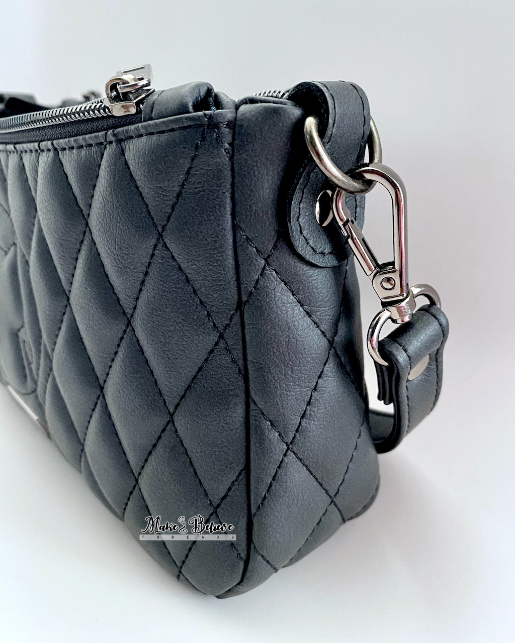 Gusset view of a quilted charcoal black shoulder bag with gunmetal strap hardware on a white background