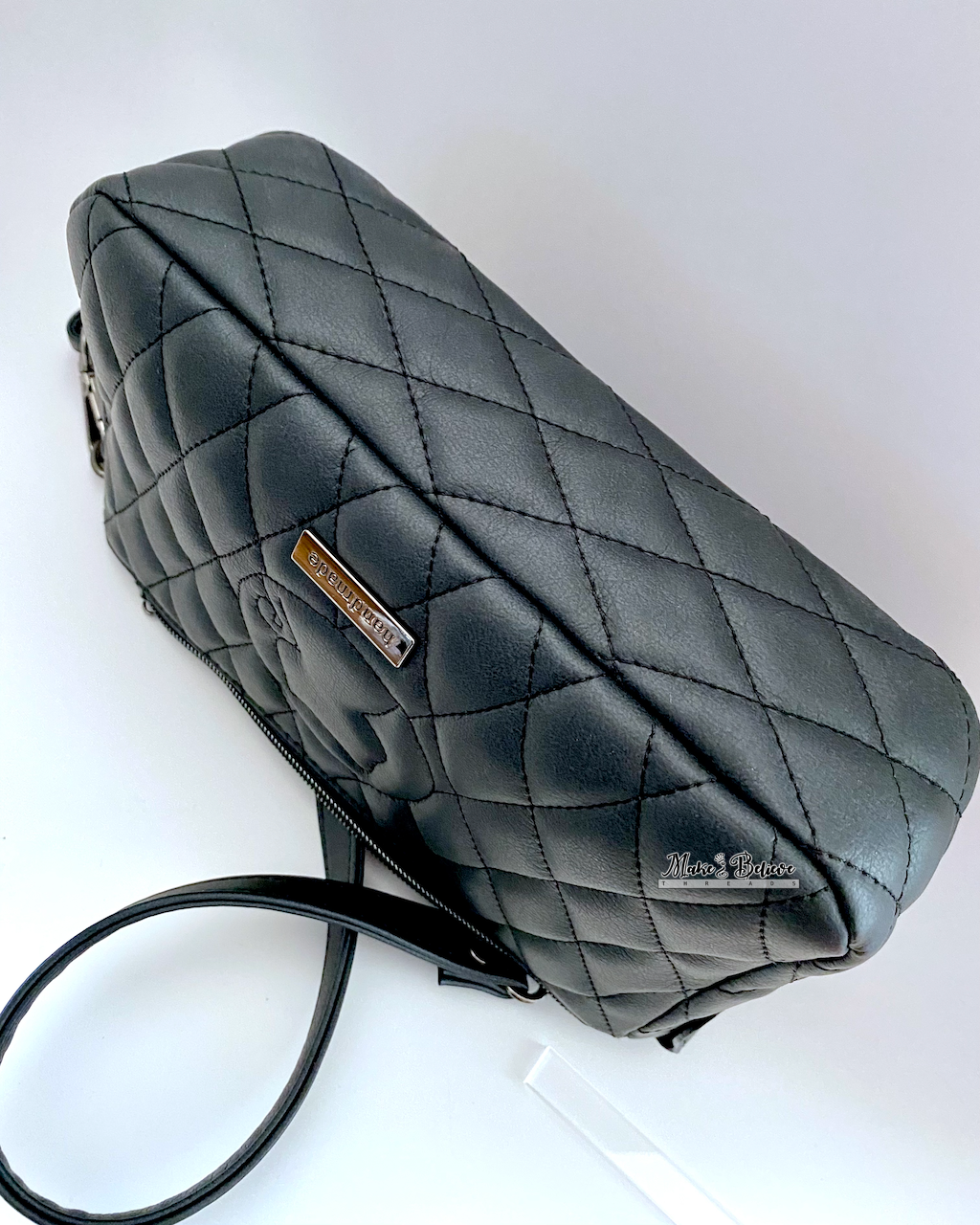 Bottom view of a charcoal black shoulder bag with diamonds quilted on all panels, photographed with a white background