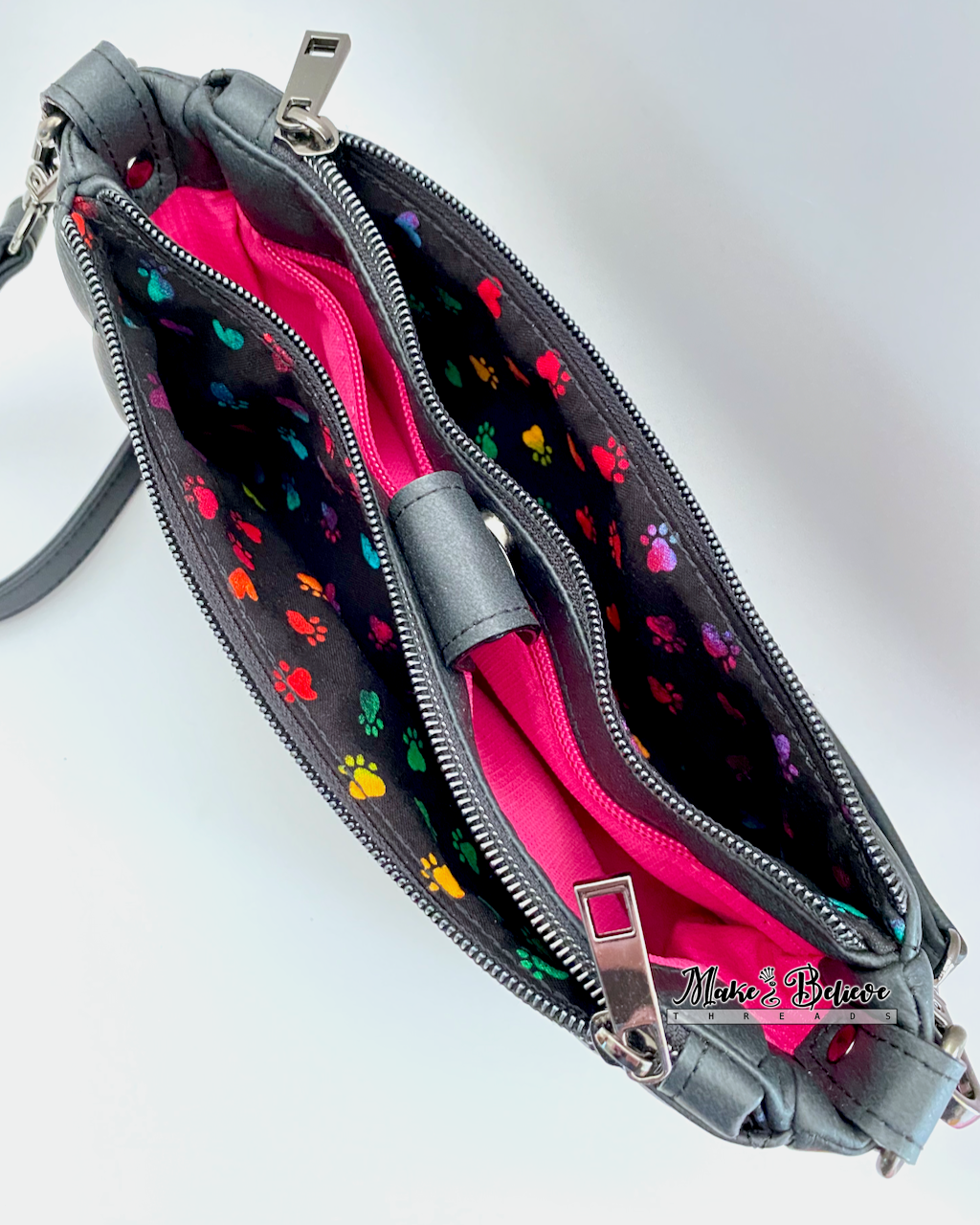 Top view of black shoulder bag with two open zipper pockets revealing colorful paw print pattern on a white background