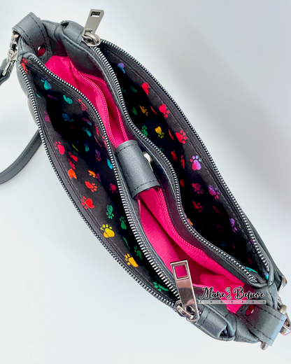 Top view of black shoulder bag with two open zipper pockets revealing colorful paw print pattern on a white background