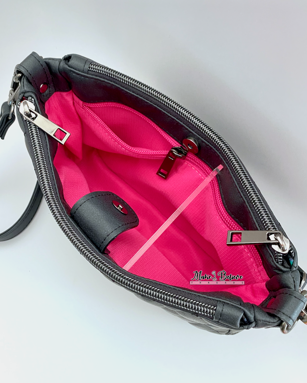 Top view of open black bag revealing gusset snap closure with pink interior and zipper pocket on a white background