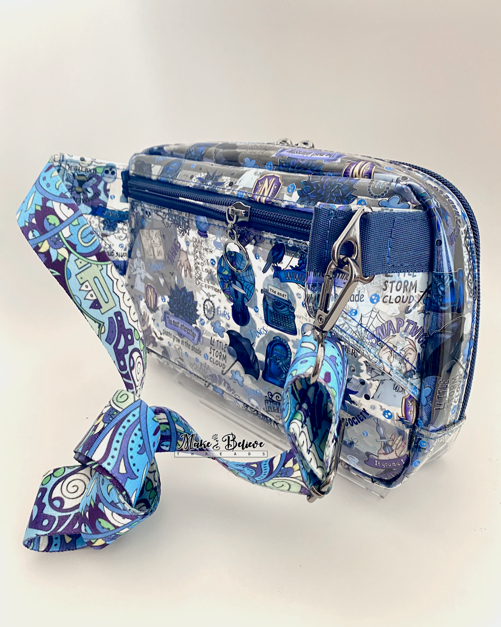 Back view of a transparent hip pack with blue accents and Wednesday icons. The view features the gunmetal side connectors and the back zipper pocket. Photographed on a white background.