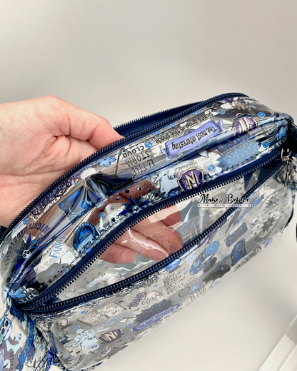 Hand inside the main zipper compartment of a clear pouch. The back zipper compartment is also open and the hand is visible through the layer that separates the two compartments. Photographed on a white background.