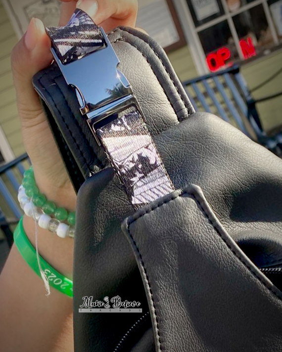 Close-up of a person holding a black faux leather bag with a metallic buckle held by Batman webbing.