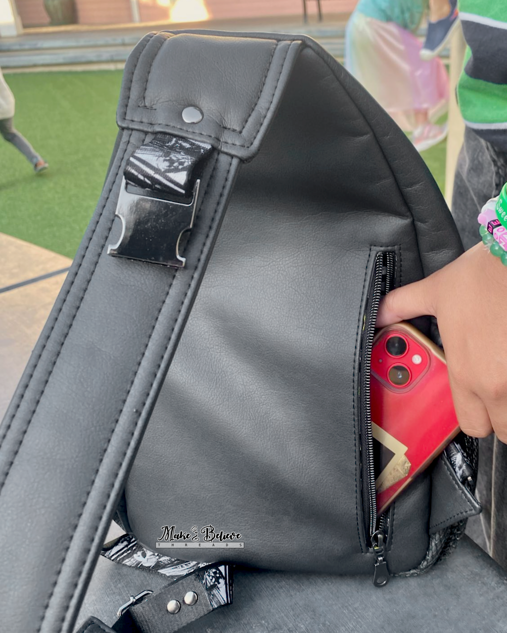 Person placing a red phone into a black faux leather backpack outdoors.