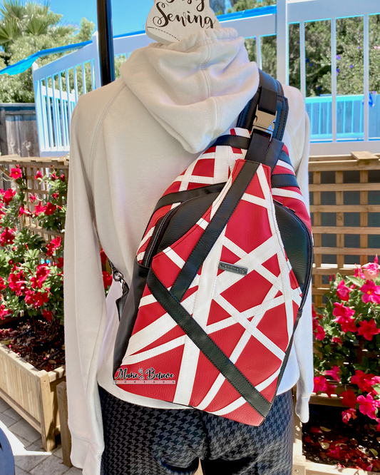 Mannequin wearing a red, white, and black sling bag outdoors with a blurred background. The geometric appliqué design is patterned after Eddie Van Halen's Frankenstrat. 
