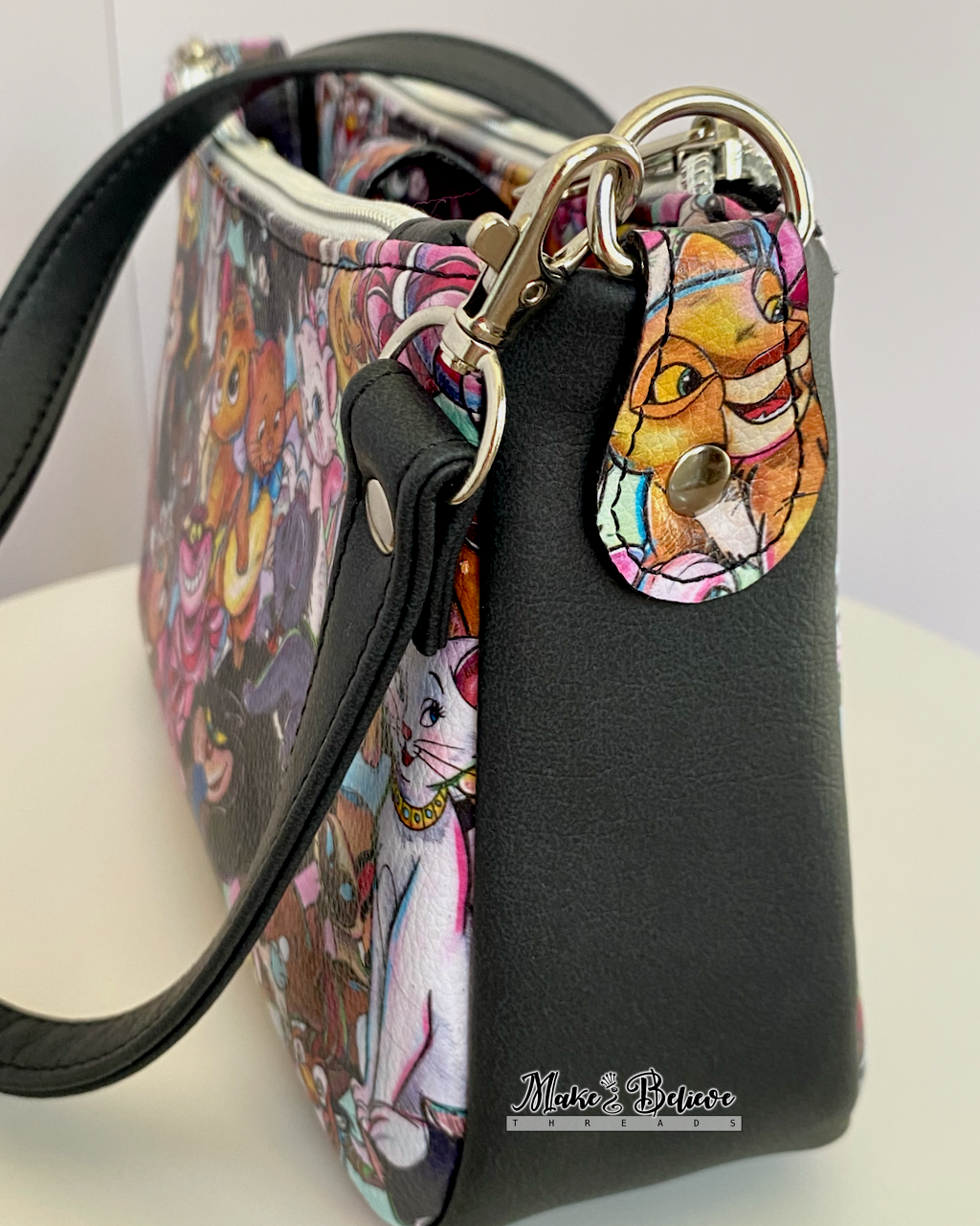 Side view of a shoulder bag with a fussy-cut baby lion face on the bag connector, photographed on white background.