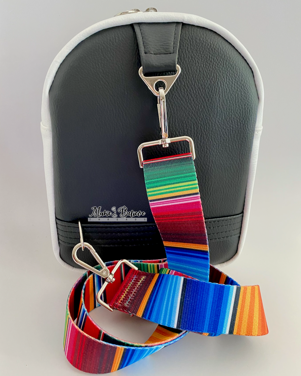 Black of sneaker shaped bag bag with a colorful striped crossbody strap and nickel hardware on a gray background