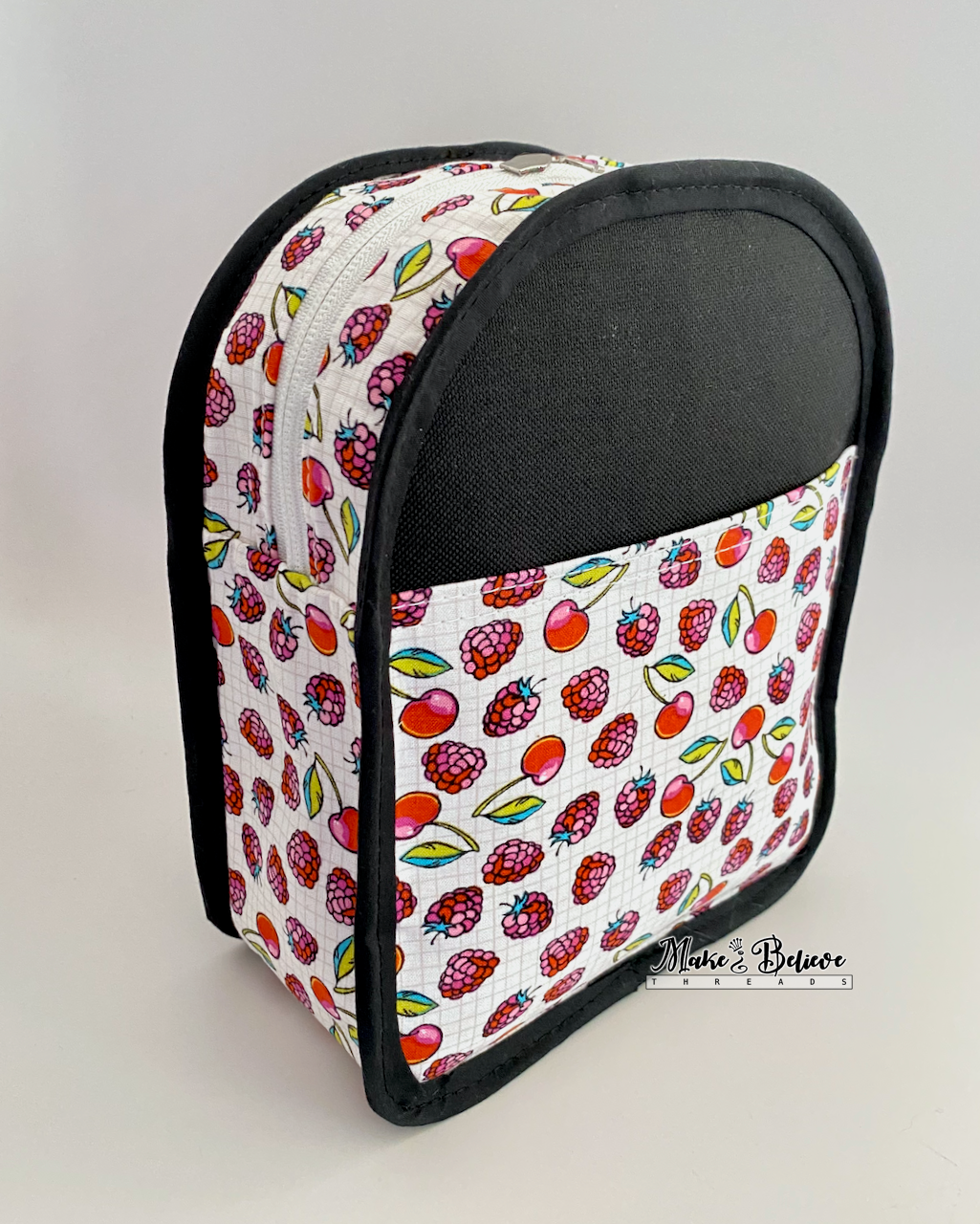 Inside out view of a small sling bag  with colorful fruit-patterned fabric and black binding on a white background