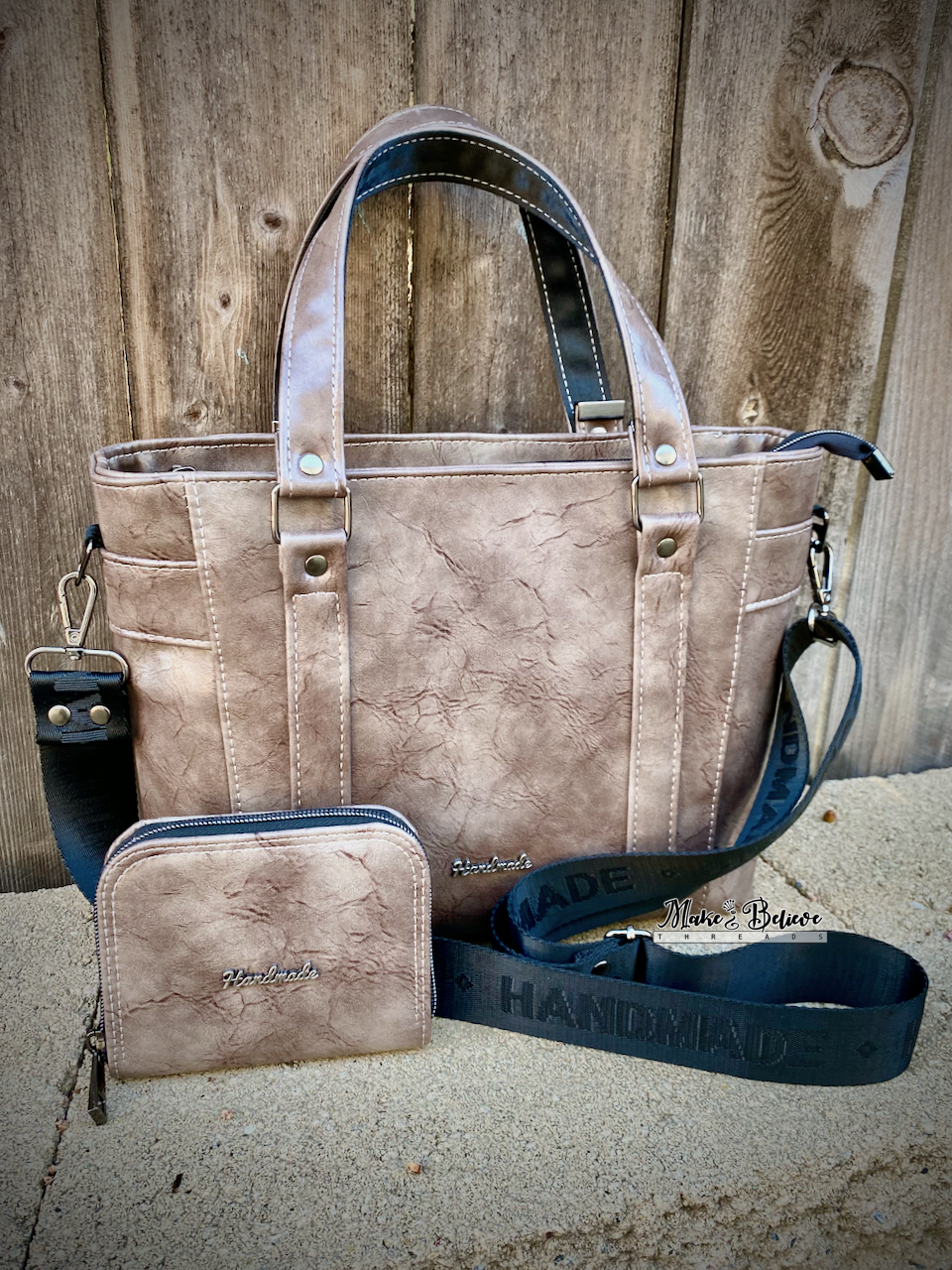 Brown-ish gray faux leather handbag and matching mini zip-around wallet with 'Handmade' strap on a stone surface