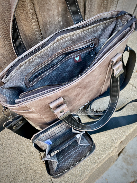 Open brownish-gray faux leather bag and mini zip-around wallet with visible interior on a stone surface