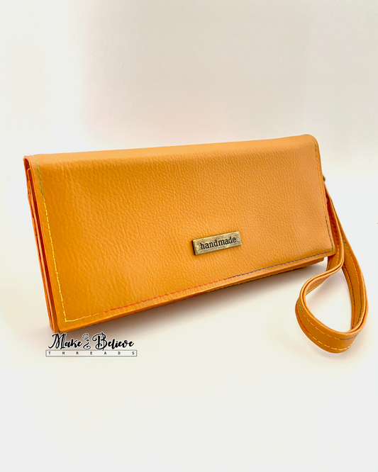 Front of ochre bookish wallet with a strap on a neutral background, featuring 'Handmade' label