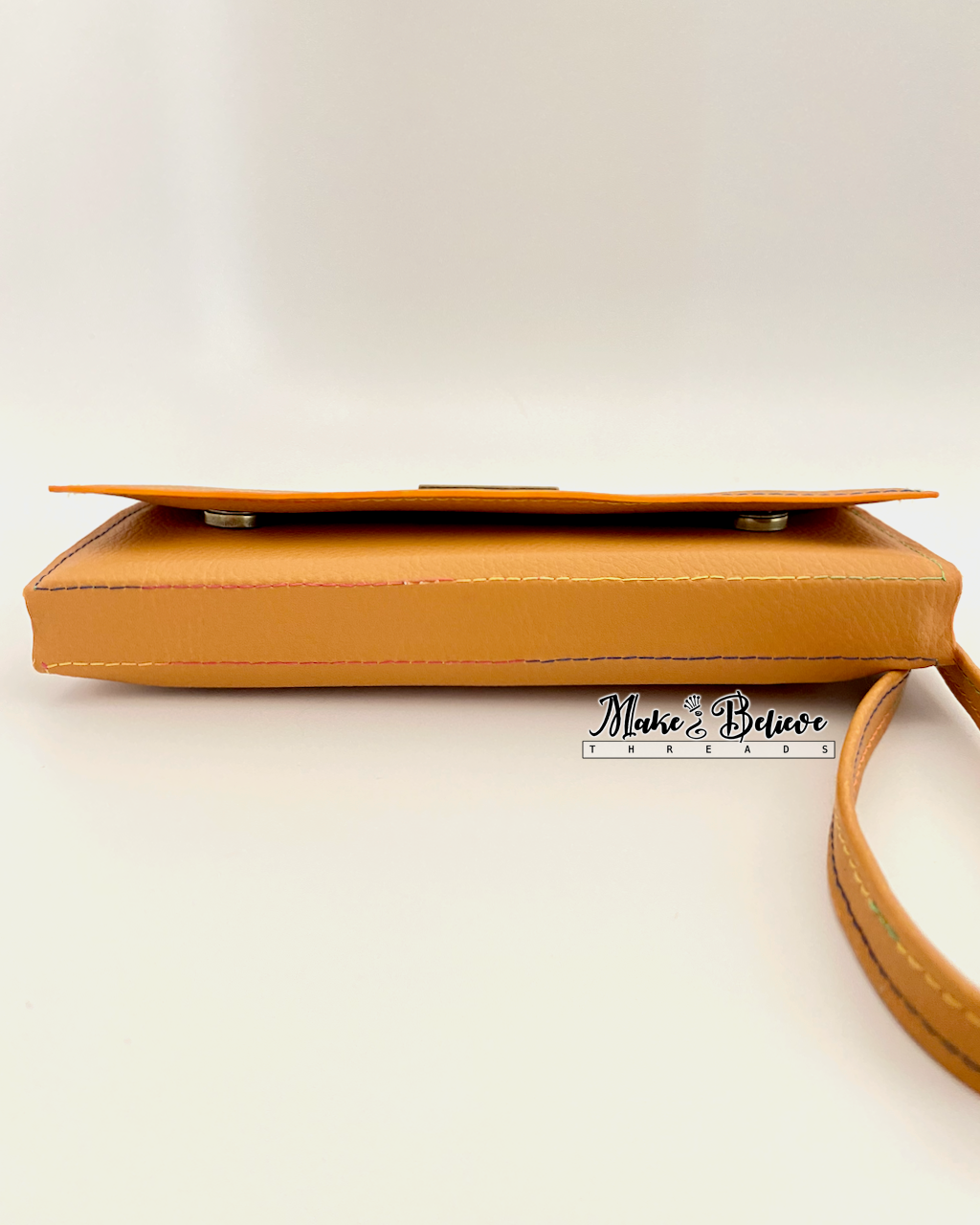 Bottom view of ochre tri-fold wallet revealing magnetic snap closures on a neutral background