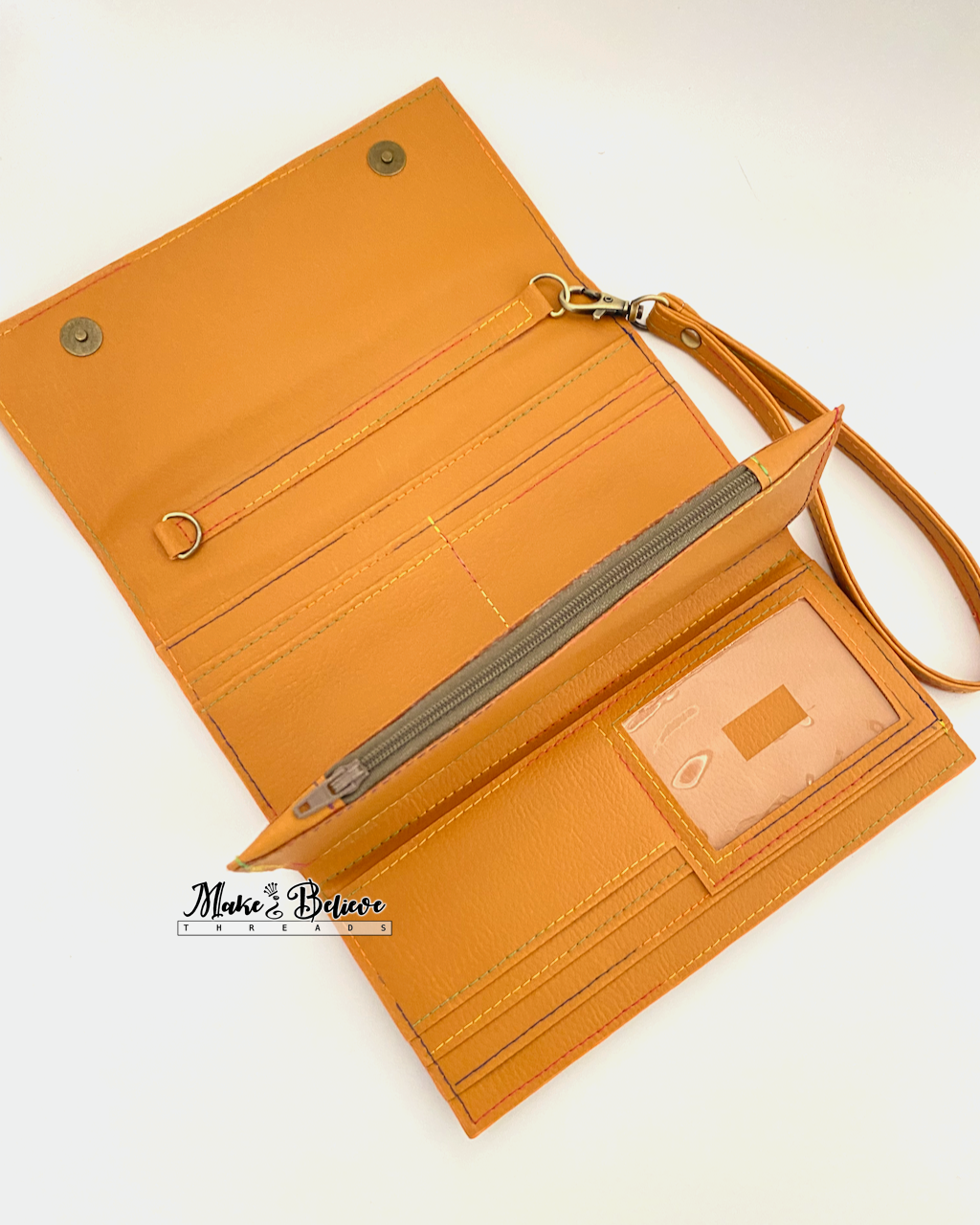 Open view of ochre tri-fold wallet showing interior wristlet connector, credit card slots, ID window, and zipper pocket on a neutral background