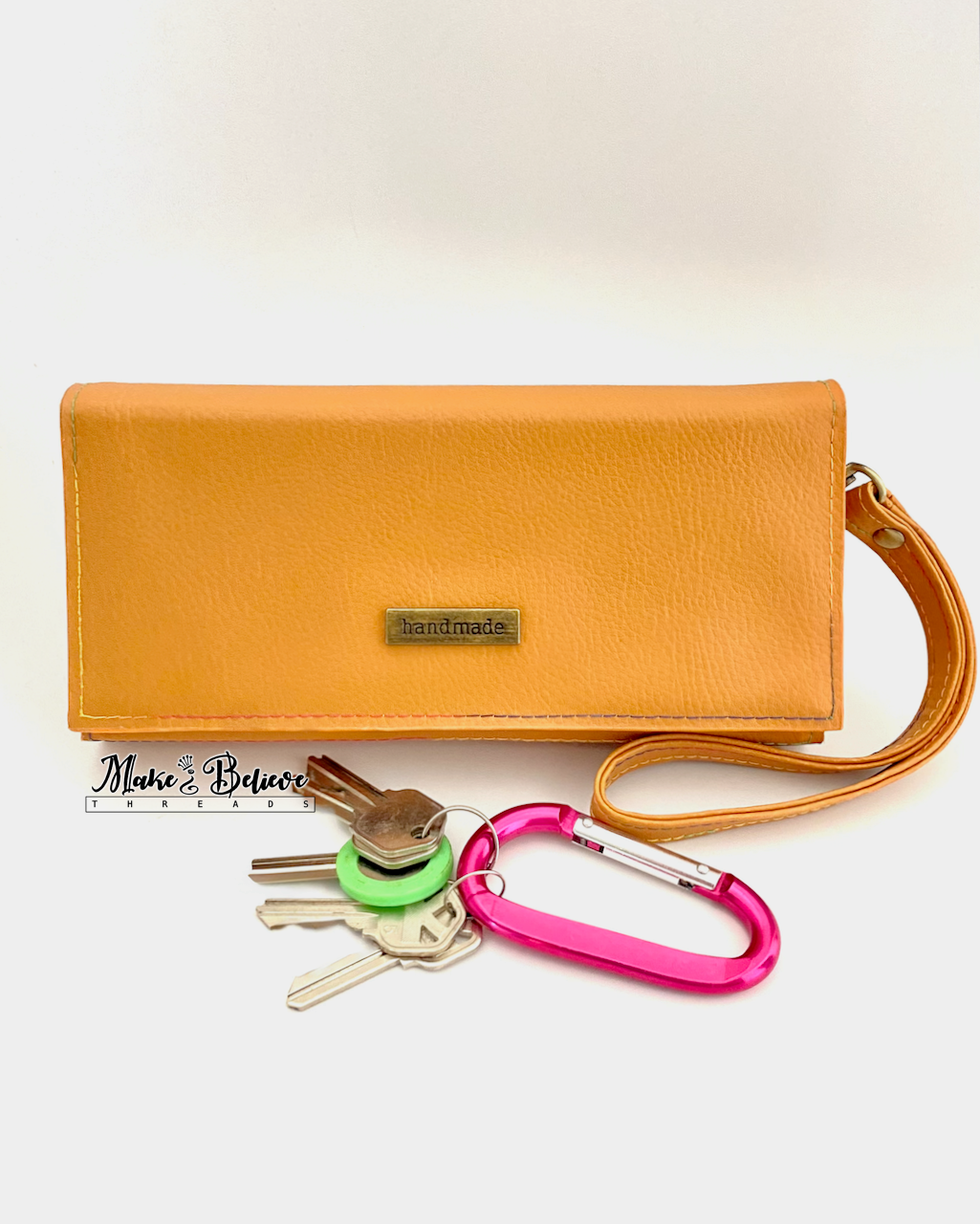Front of ochre bookish wallet with a strap on a neutral background, photographed with a set of keys for scale