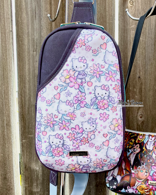 Purple sling bag with pastel floral "Bow Kitty" design on a wooden background.