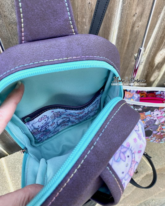 Close-up of a purple and turquoise bag with a pastel floral "Bow Kitty" slip pocket, held open by a hand.