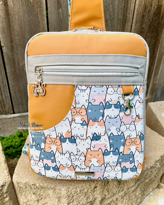 Medium-sized rectangular sling bag with cat pattern and orange top section on a stone surface.