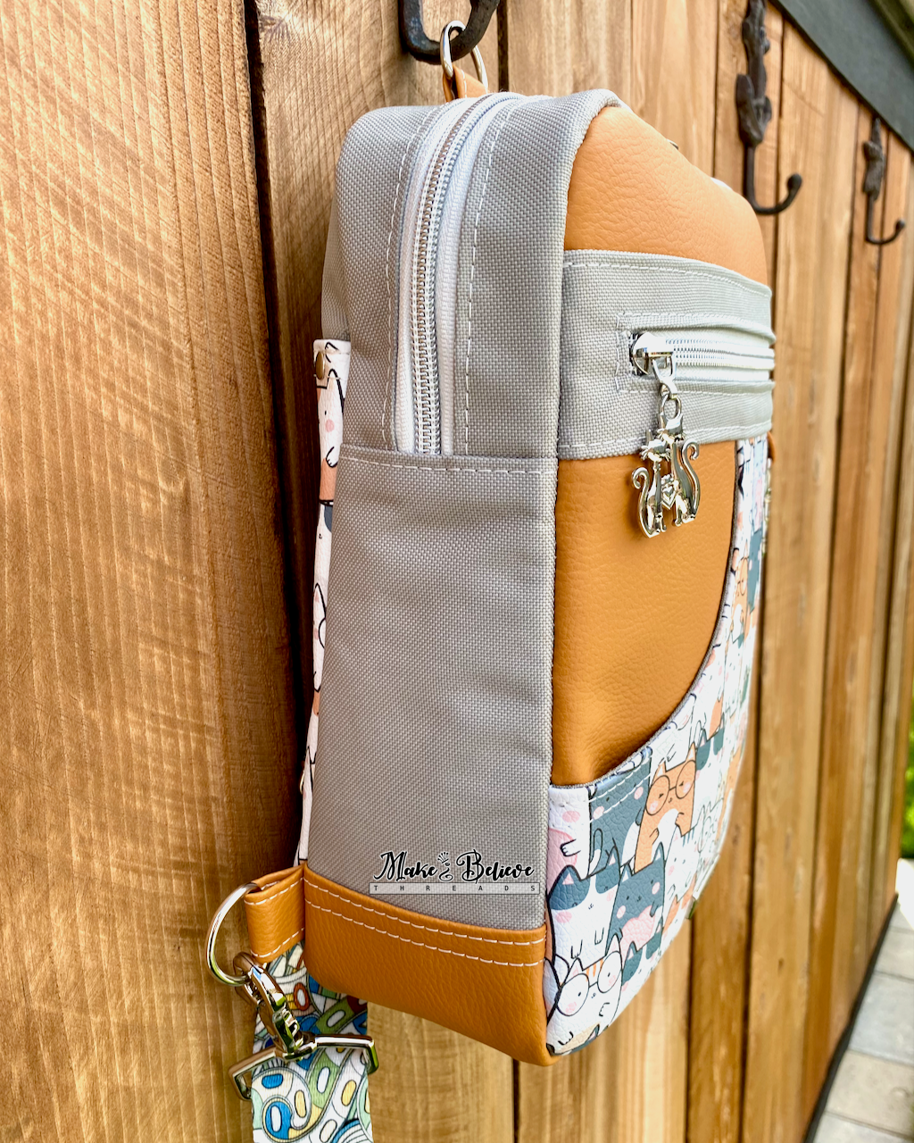 Side view of the gray gusset on a burnt orange sling bag with zipper and slip pockets hanging on a wooden surface