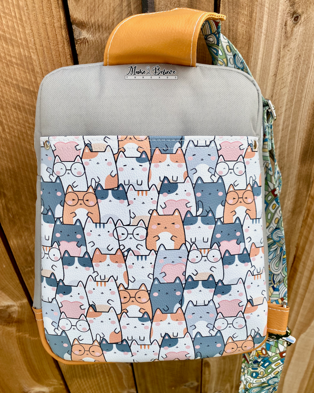Sling with cat patterned slip pocket on back panel against a wooden background