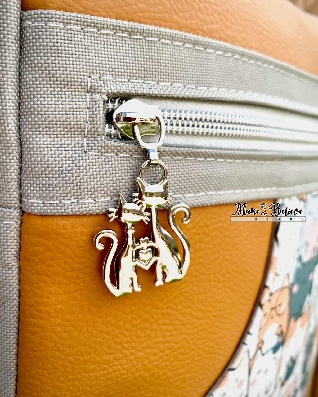 Close-up of nickel cat-shaped zipper pull on a burnt orange and gray sling bag