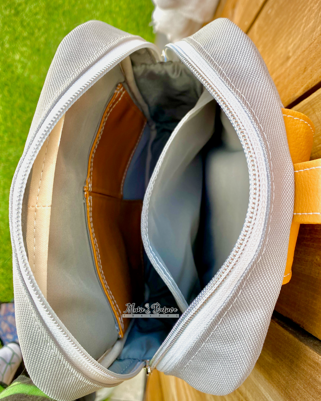 Close-up of 3 slip pockets in the interior of a gray and burnt orange sling bag against a wood surface.