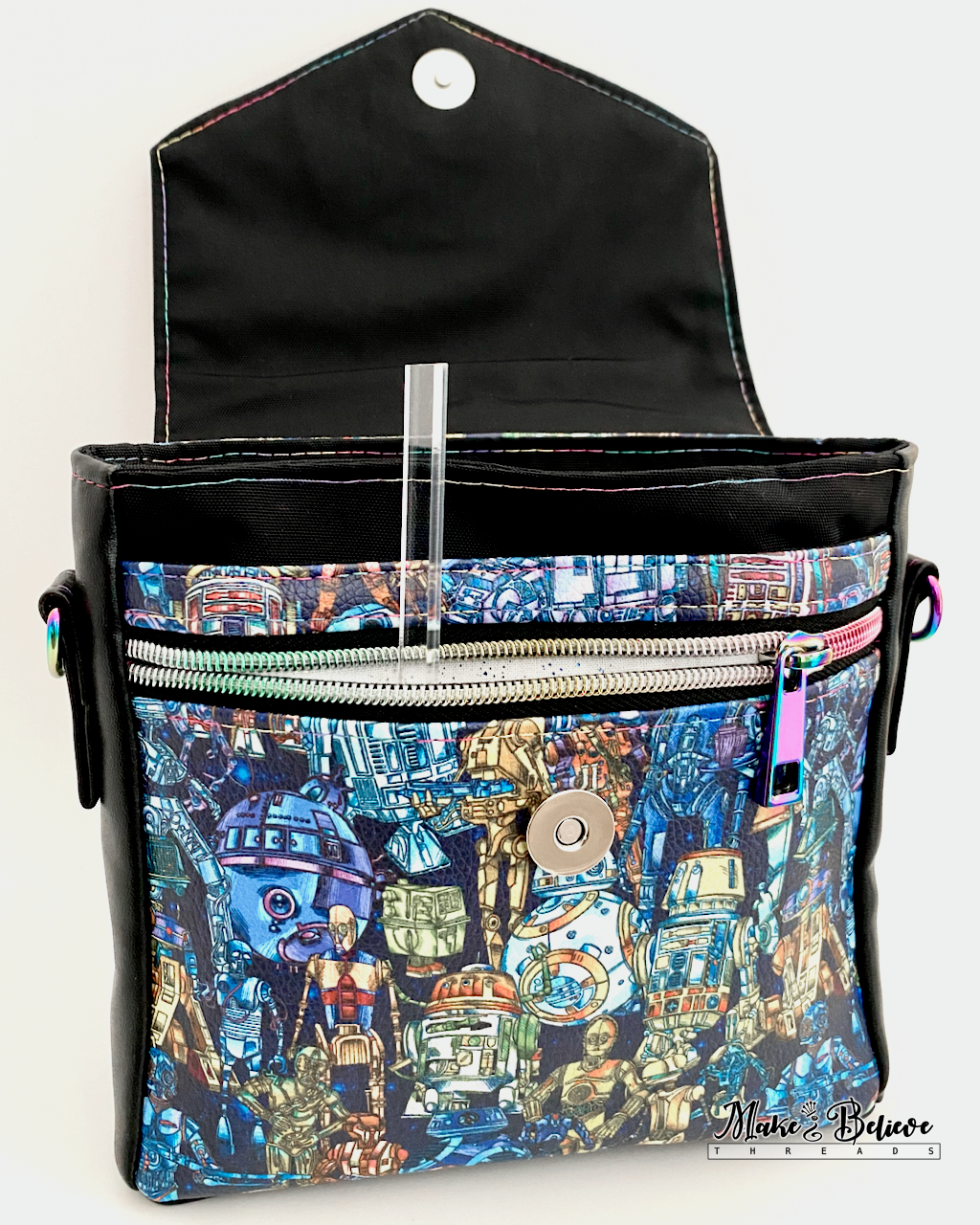Opened flap of black faux leather bag revealing space wars droids printed vinyl panel and both a zipper and slip pocket on a white background