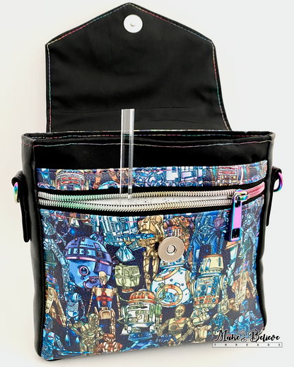 Opened flap of black faux leather bag revealing space wars droids printed vinyl panel and both a zipper and slip pocket on a white background